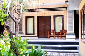 A building with a stone facade, a wooden door, and a small outdoor seating area with two chairs. - Putu Guest House 2 (Tibubeneng)