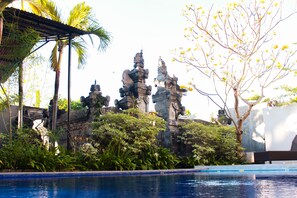 A pool area with stone statues and tropical vegetation. - Putu Guest House 2 (Tibubeneng)