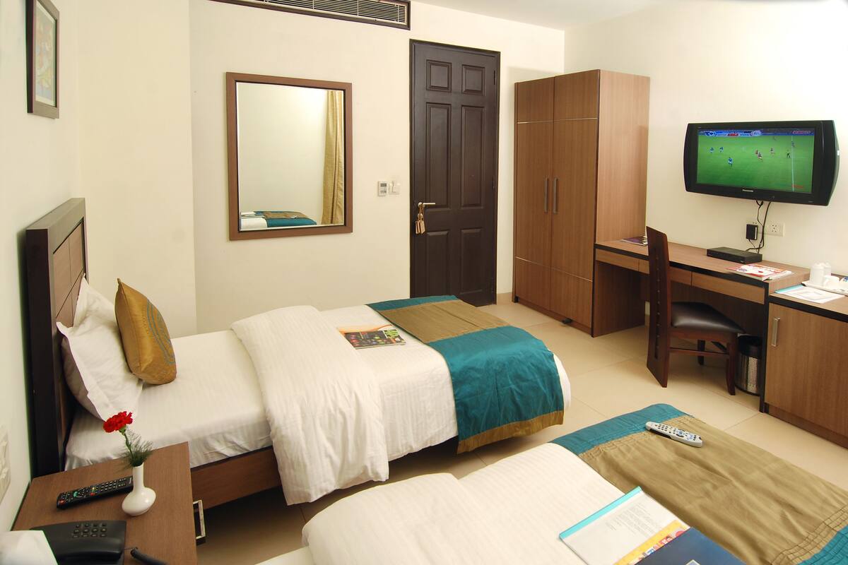 Habitación de hotel con dos camas, un escritorio, un televisor y un espejo.
