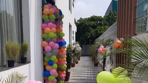 A corridor with a row of colorful balloons on one side and potted plants on the other. - Silver Ark (Gurugram)