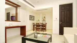 A modern living room with a glass coffee table, a dining area with wooden chairs, a dark wooden door, and a white sofa. - Silver Ark (Gurugram)