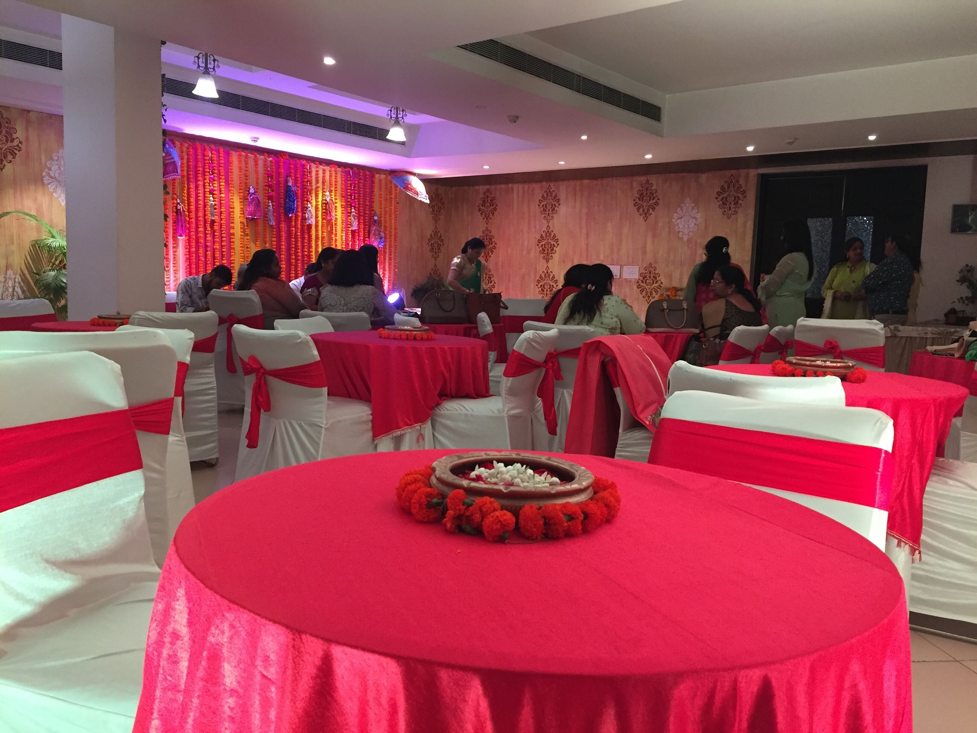 A banquet hall with round tables covered in red cloths, white chairs with red sashes, and a floral centerpiece.