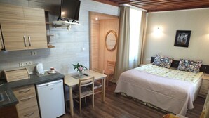 Habitación de hotel compacta con kitchenette, cama con ropa de cama estampada, una pequeña mesa de comedor y una sola silla.