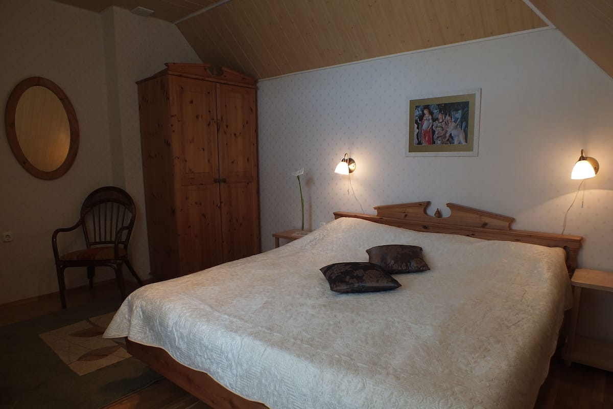 Ein Schlafzimmer mit einem hölzernen Bett, zwei Kissen, einem Nachttisch, einem Holzschrank, einem Stuhl und einem an der Wand hängenden Gemälde.