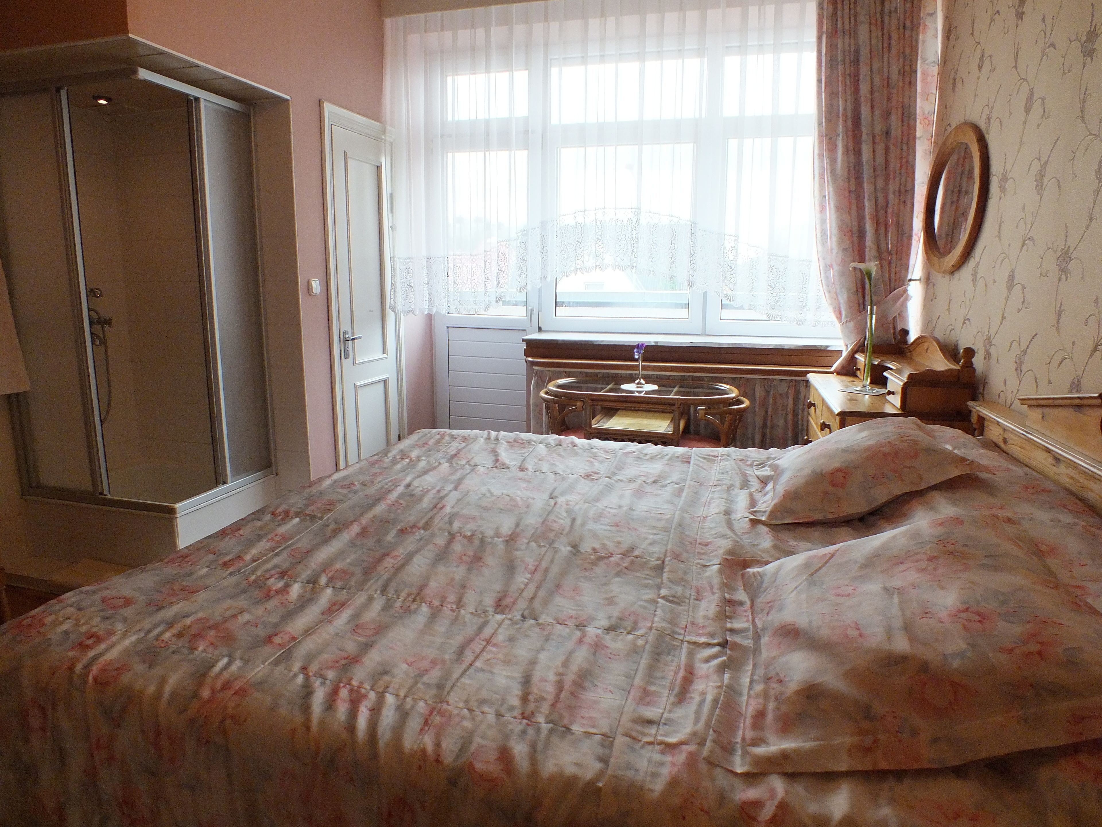 Ein Schlafzimmer mit einem Bett, einem Schminktisch mit Spiegel, einem Fenster mit durchsichtigen Vorhängen und einem Kleiderschrank.