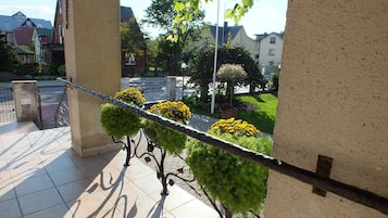A balcony with tiled flooring, a metal railing, and potted plants with yellow flowers.