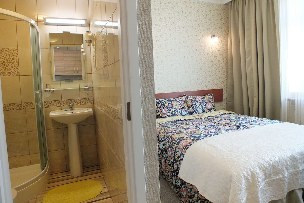 Ein Hotelzimmer mit Dusche, Waschbecken und einem Bett mit floralem Überwurf.