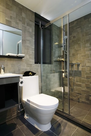 A modern bathroom with a white toilet, a glass shower enclosure, and a tiled wall. - M1 Hotel North Point (Hong Kong Island)