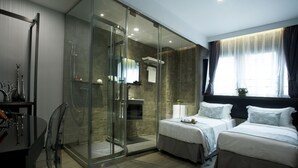 Une chambre d’hôtel moderne dotée d’une douche en verre, de deux lits, d’un bureau et d’une grande fenêtre avec des rideaux.