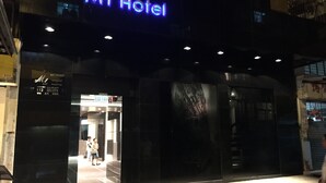L’extérieur du Mi Hotel se distingue par une enseigne au néon, une entrée avec des portes vitrées et un escalier bien visible menant à l’entrée.