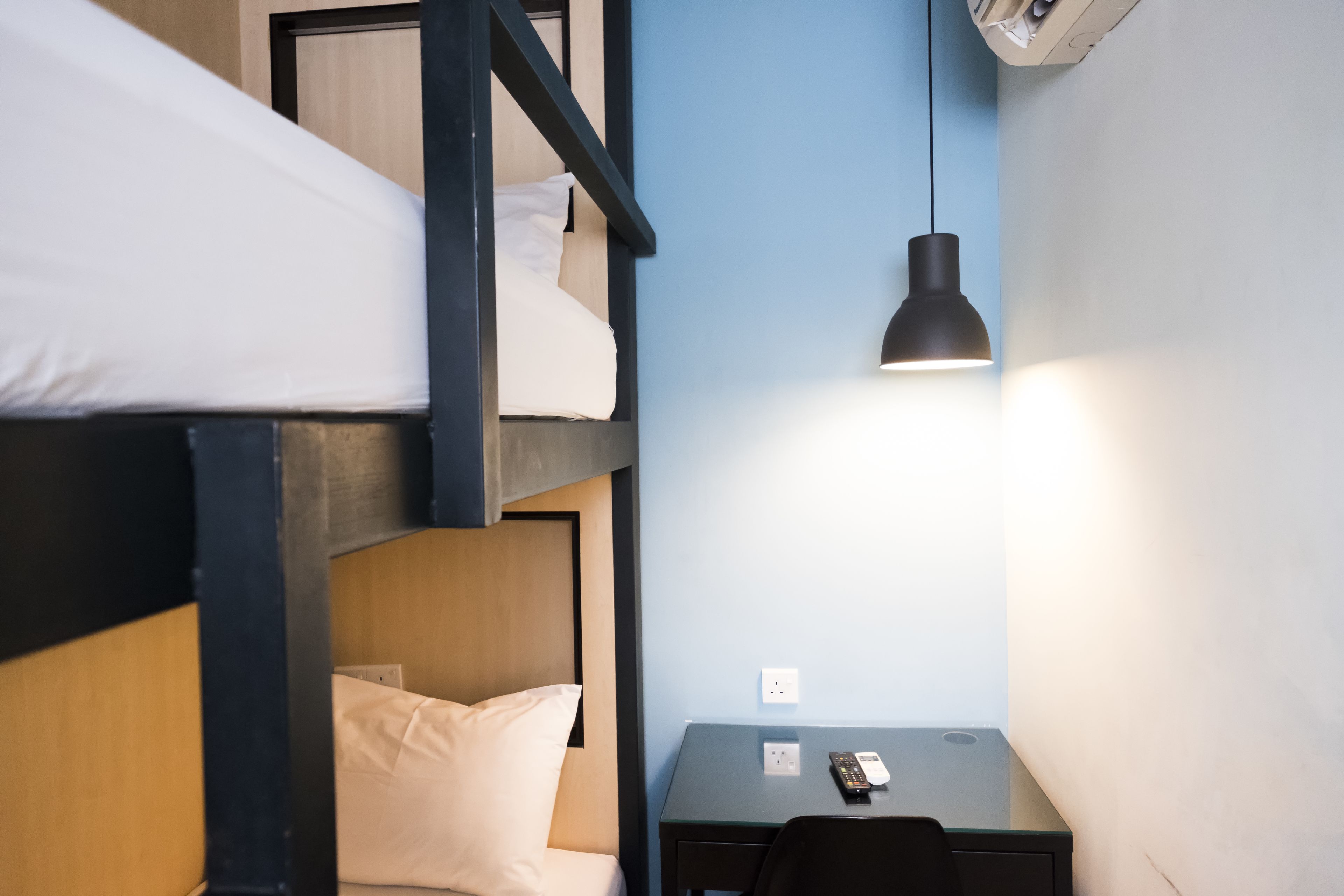 A bunk bed room with a desk and a hanging lamp.