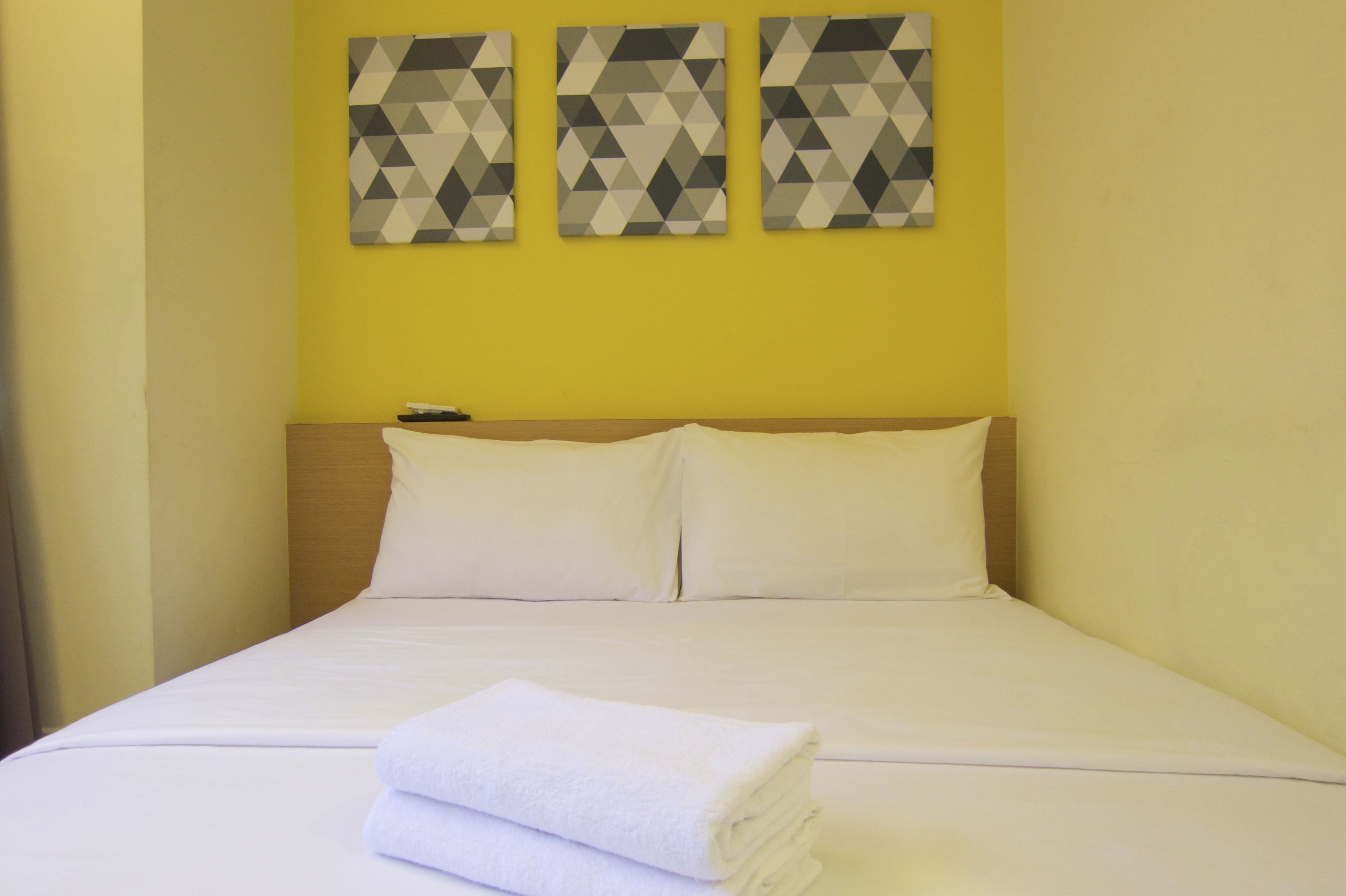 A hotel room with a bed, white linens, a folded towel, and three geometric-patterned wall art pieces.