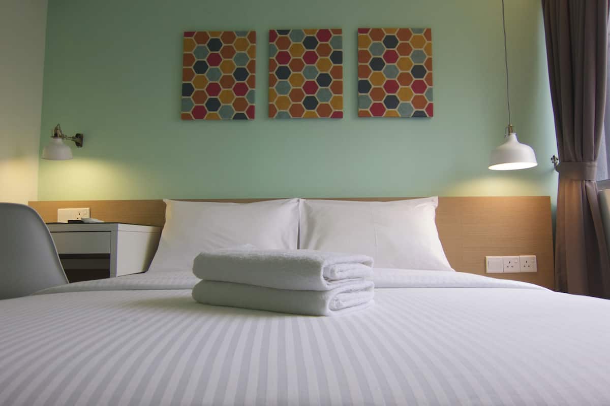A neatly made bed with white linens and a folded towel, a bedside table with a lamp, and three hexagonal-patterned wall art pieces above the bed.