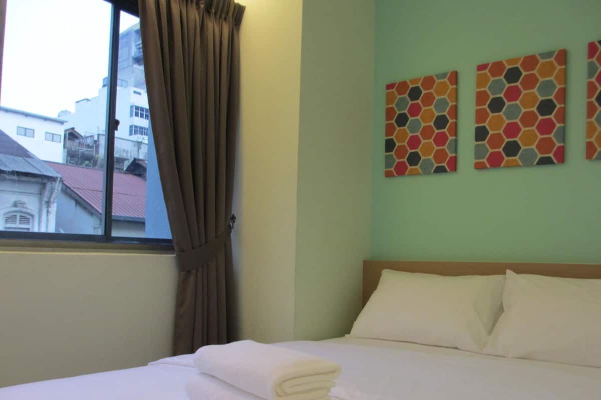 A hotel room with a bed, a window with curtains, and three colorful hexagonal wall art pieces.