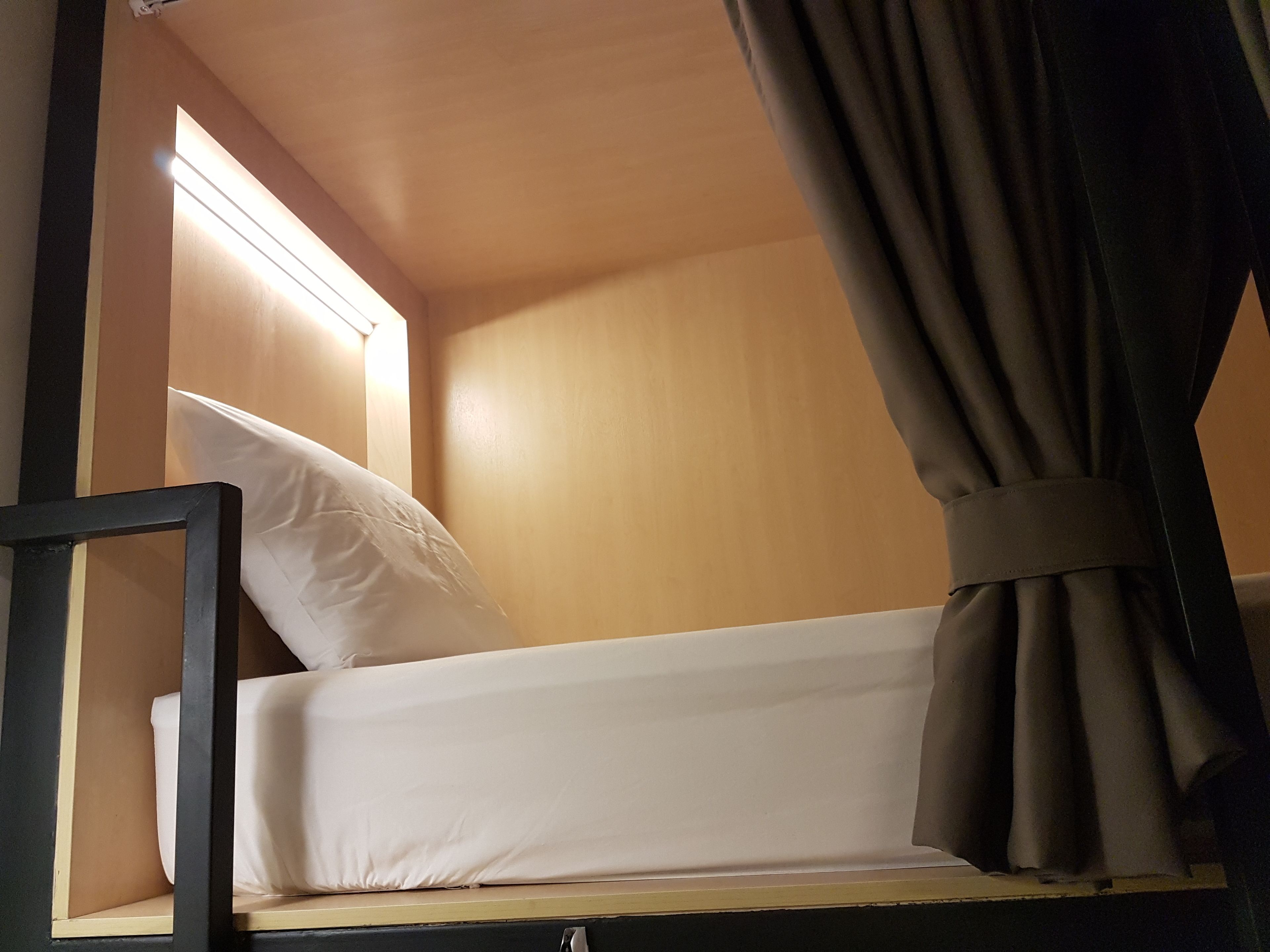 Una cama litera con ropa de cama blanca, un cabecero de madera y una cortina a la derecha.