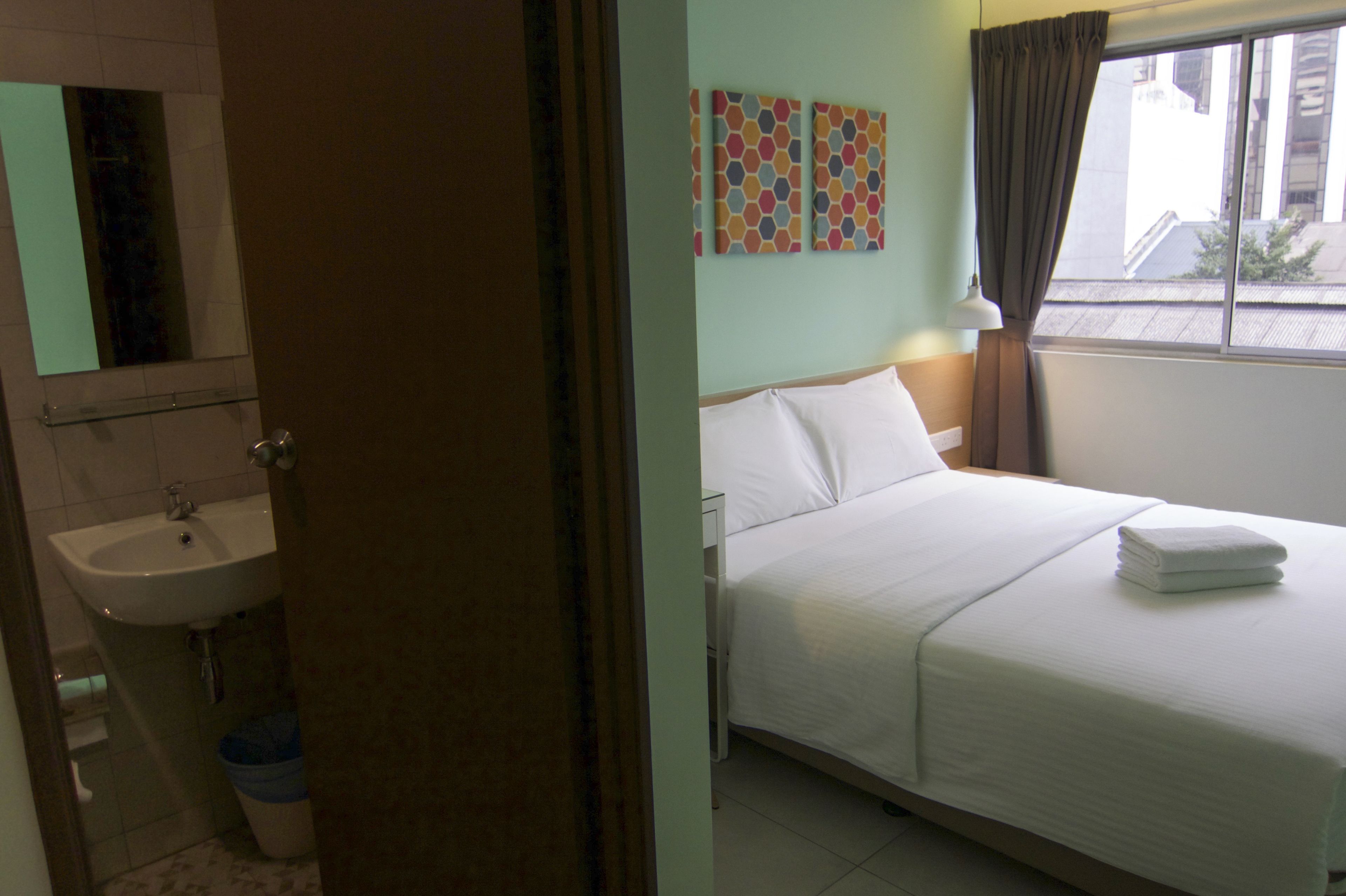A hotel room with a bed, a window with curtains, a sink, and a mirror.