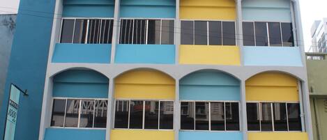 Um hotel com vários andares e fachada azul e amarela marcante, com grandes janelas em arco e entrada no nível da rua.