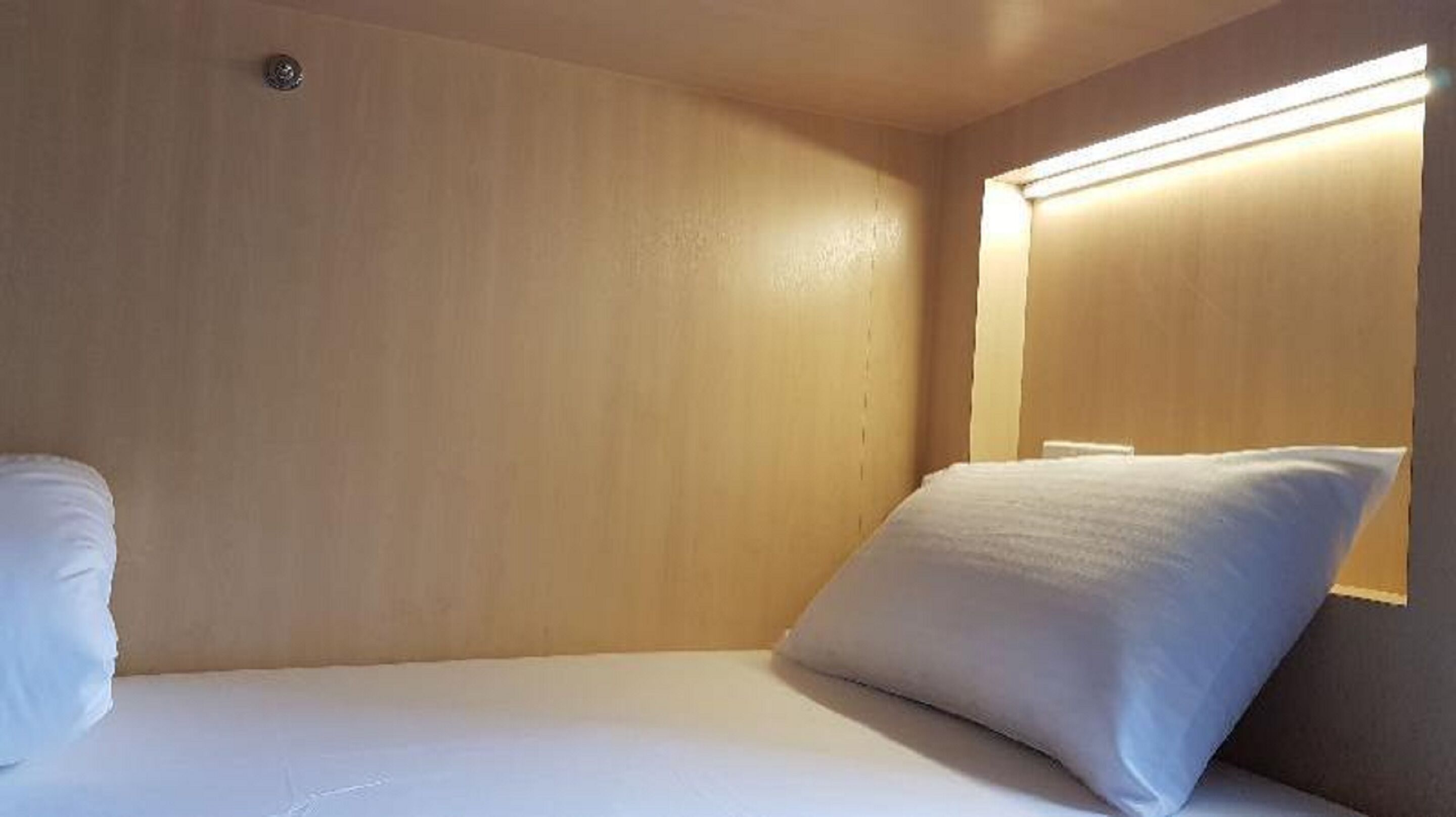 A small, single-bed room with a wooden wall and a bedside lamp.