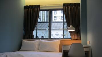 Quarto de hotel com cama, escrivaninha e janela com cortinas.