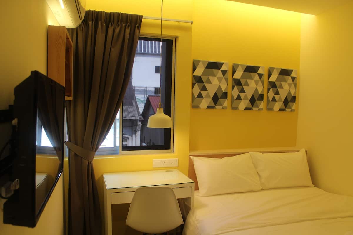 A hotel room with a bed, a desk, a chair, a window with curtains, and geometric wall art.