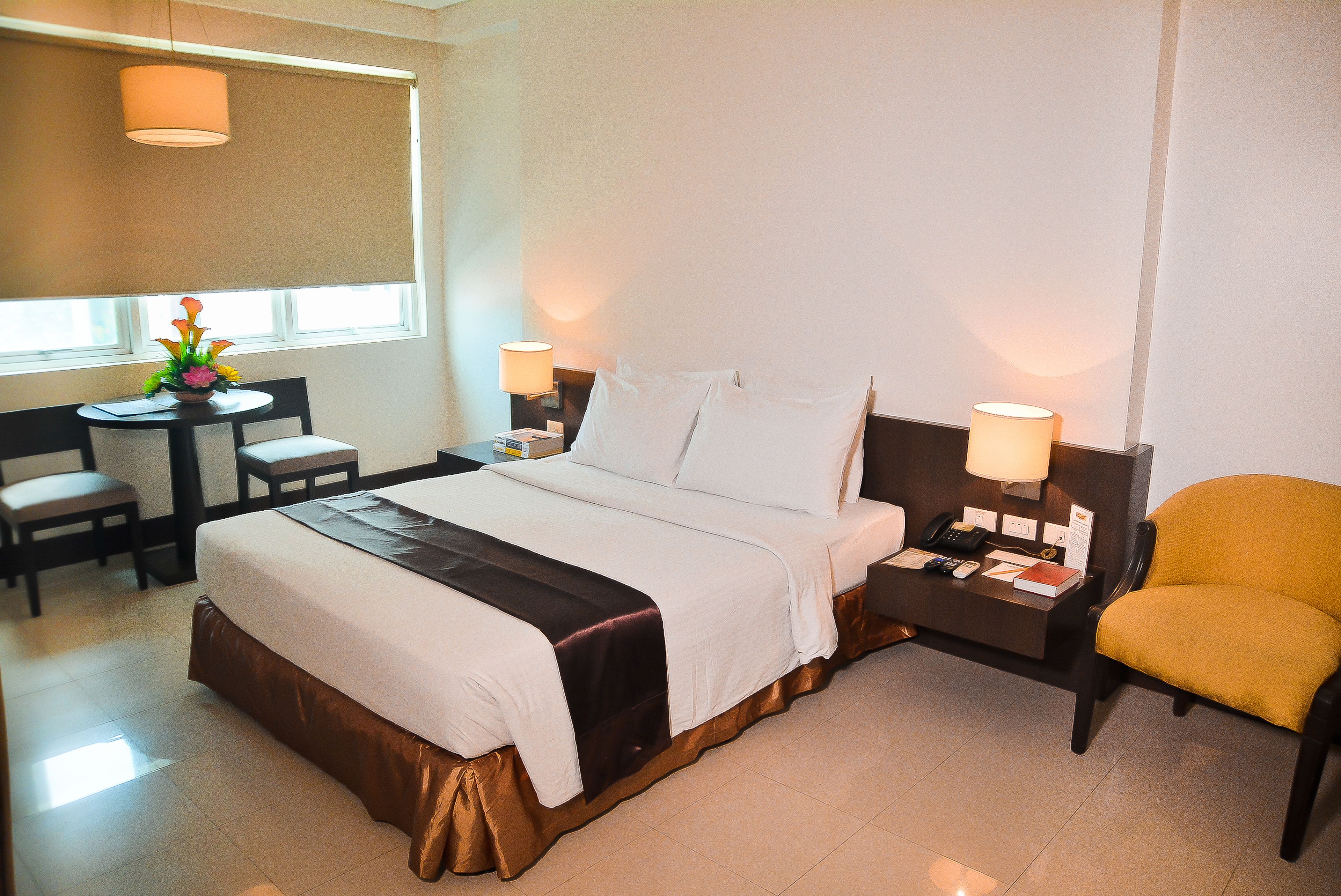 Habitación de hotel con cama, mesitas de noche, escritorio, silla y ventana con persianas.