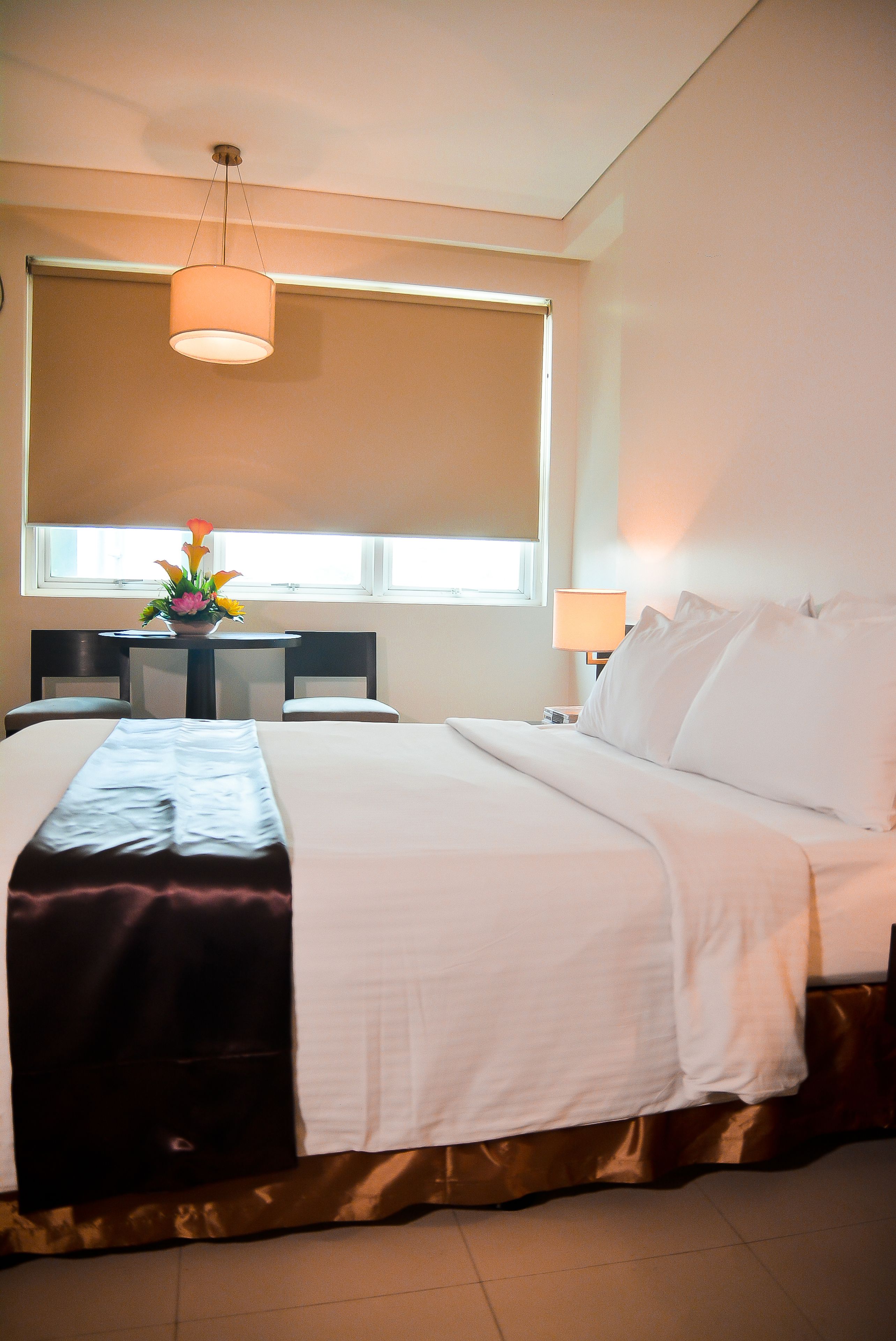 A hotel room with a large bed, a desk with a lamp, and a window with blinds.
