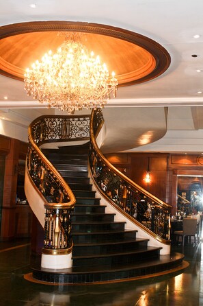 A grand spiral staircase with ornate black and gold railings, a large chandelier, and a polished wooden ceiling. - Citystate Tower Hotel (Manila)