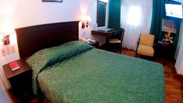 A hotel room with a large bed, a desk, a chair, and a television.