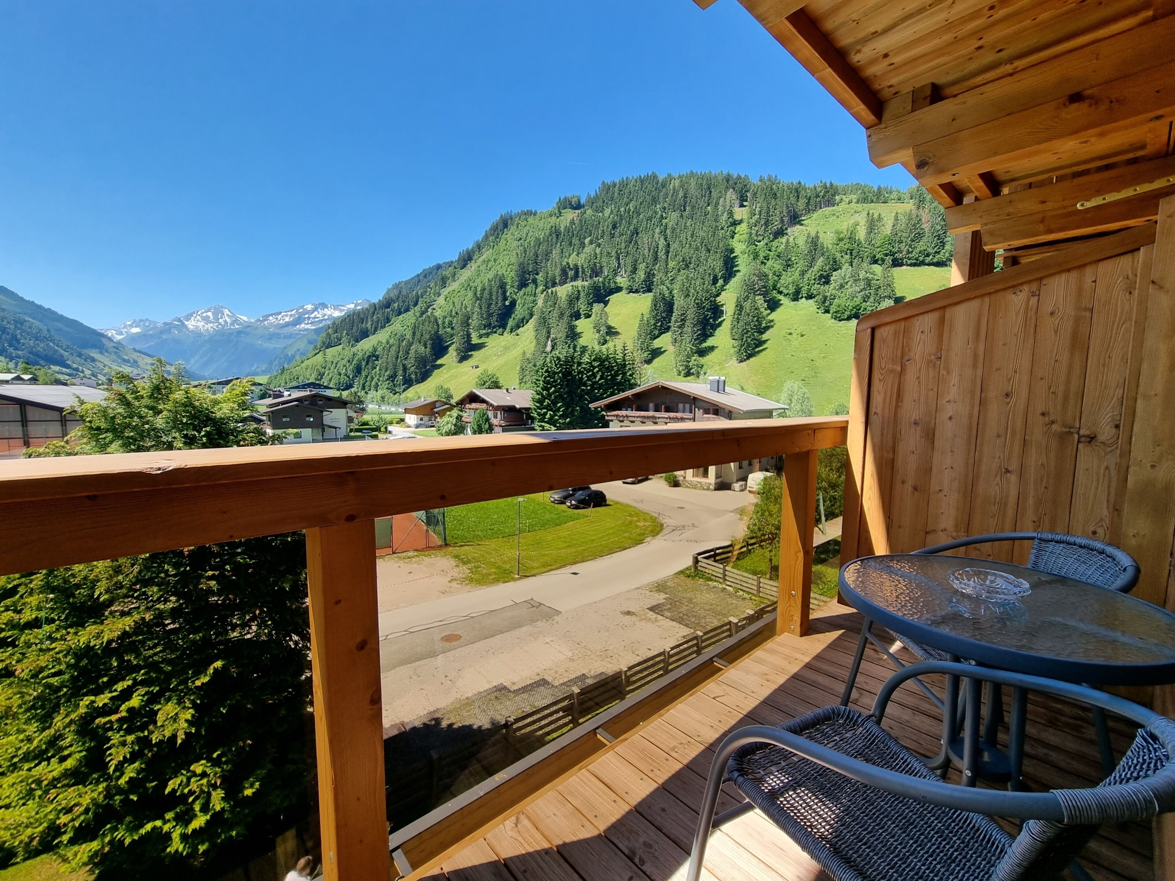A wooden deck with a glass table and chairs overlooking a mountainous landscape with houses.