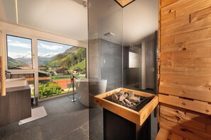 A modern bathroom with a glass shower enclosure, a wooden sauna, and a view of a mountainous landscape. - Hotel Alpina (Rauris)