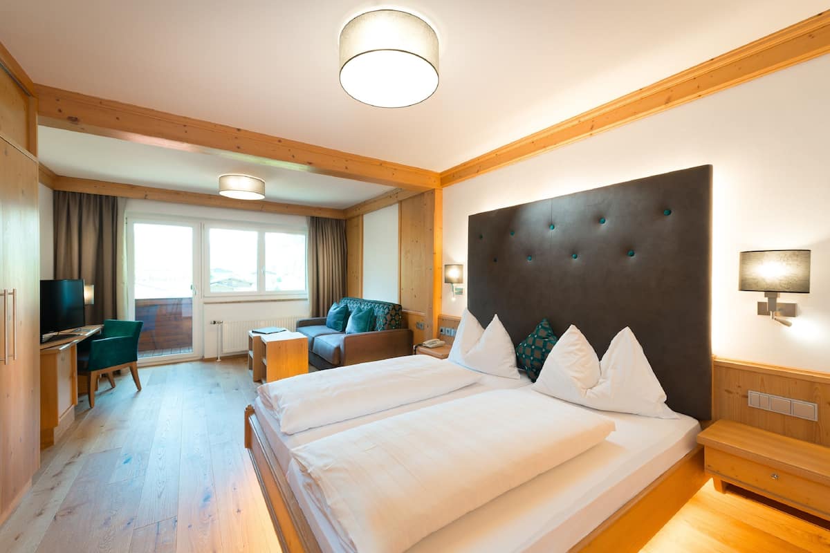 A hotel room with a large bed, a desk, a chair, and a sofa.