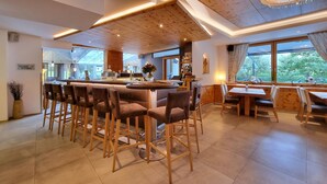 A modern restaurant with a bar area, wooden ceiling, and large windows offering a view of the outdoors. - Hotel Alpina (Rauris)