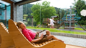 A wooden bench with a person reading a book. - Hotel Alpina (Rauris)
