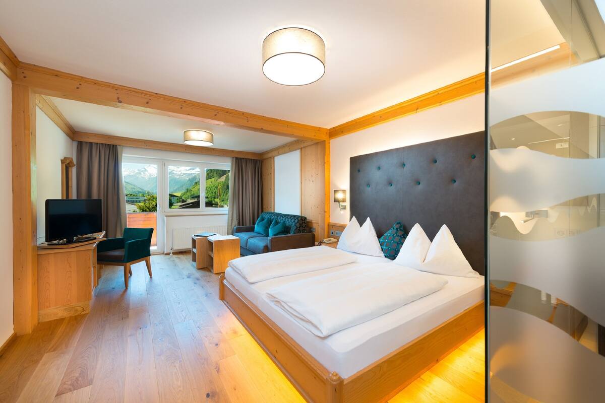 A hotel room with a large bed, a television, a sofa, and a view of mountains through the window.