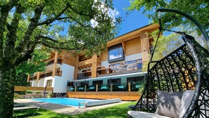 A modern two-story building with a pool, outdoor seating, and a large window overlooking the pool. - Hotel Alpina (Rauris)