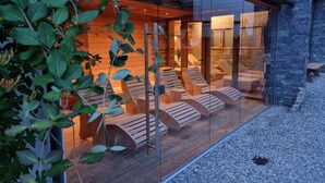 A spa area with wooden loungers and a glass enclosure. - Hotel Alpina (Rauris)