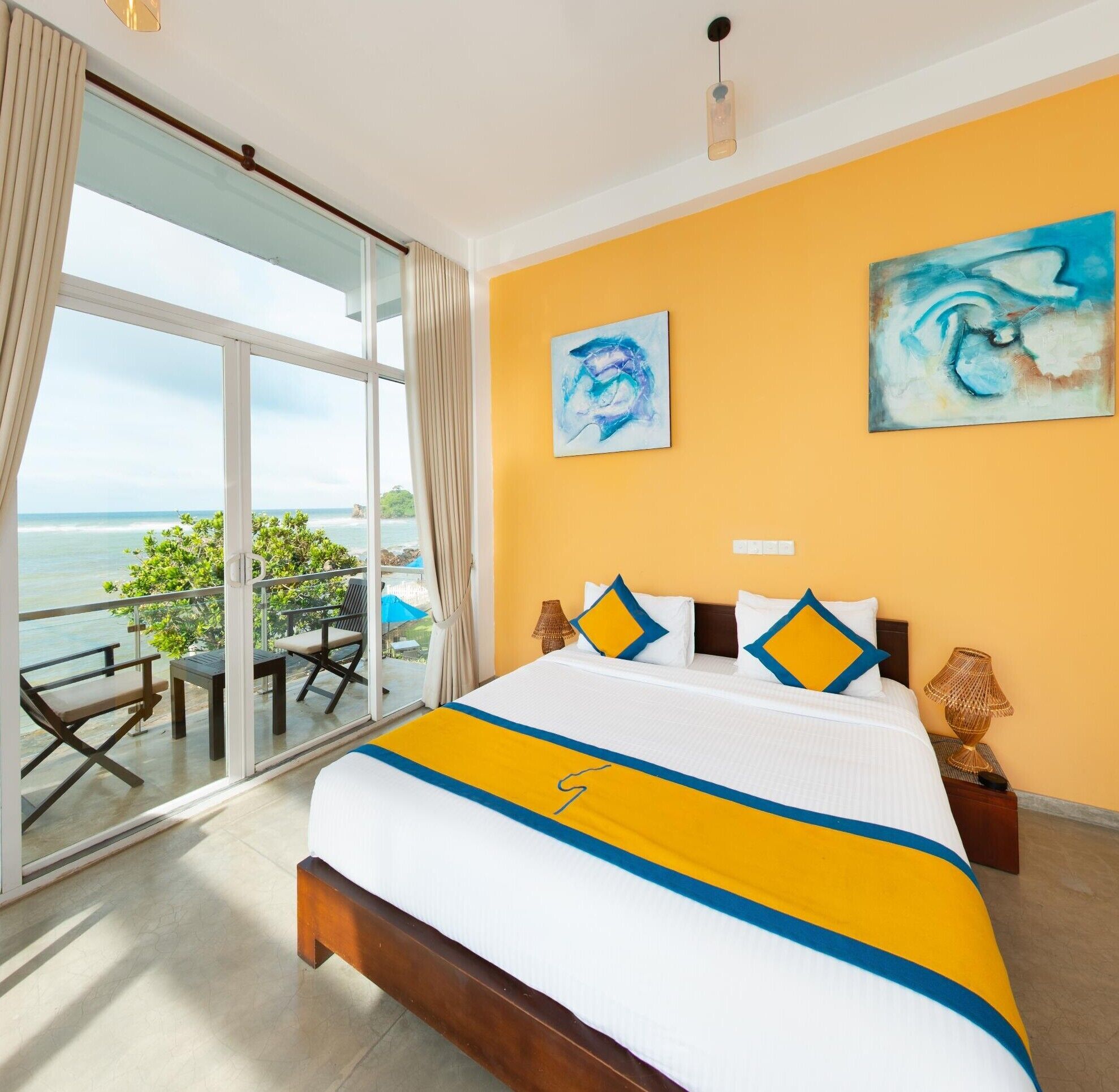 Una habitación de hotel con cama, un balcón con vista al mar y dos cuadros en la pared.