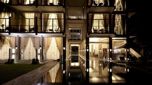 Et hotel med flere etager, et spejlbassin i forgrunden, altaner på hver etage og en godt oplyst indgang.