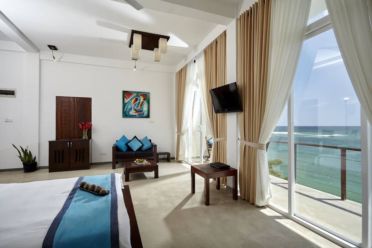 Habitación de hotel con cama, sofá, televisión, mesa y vistas al océano.