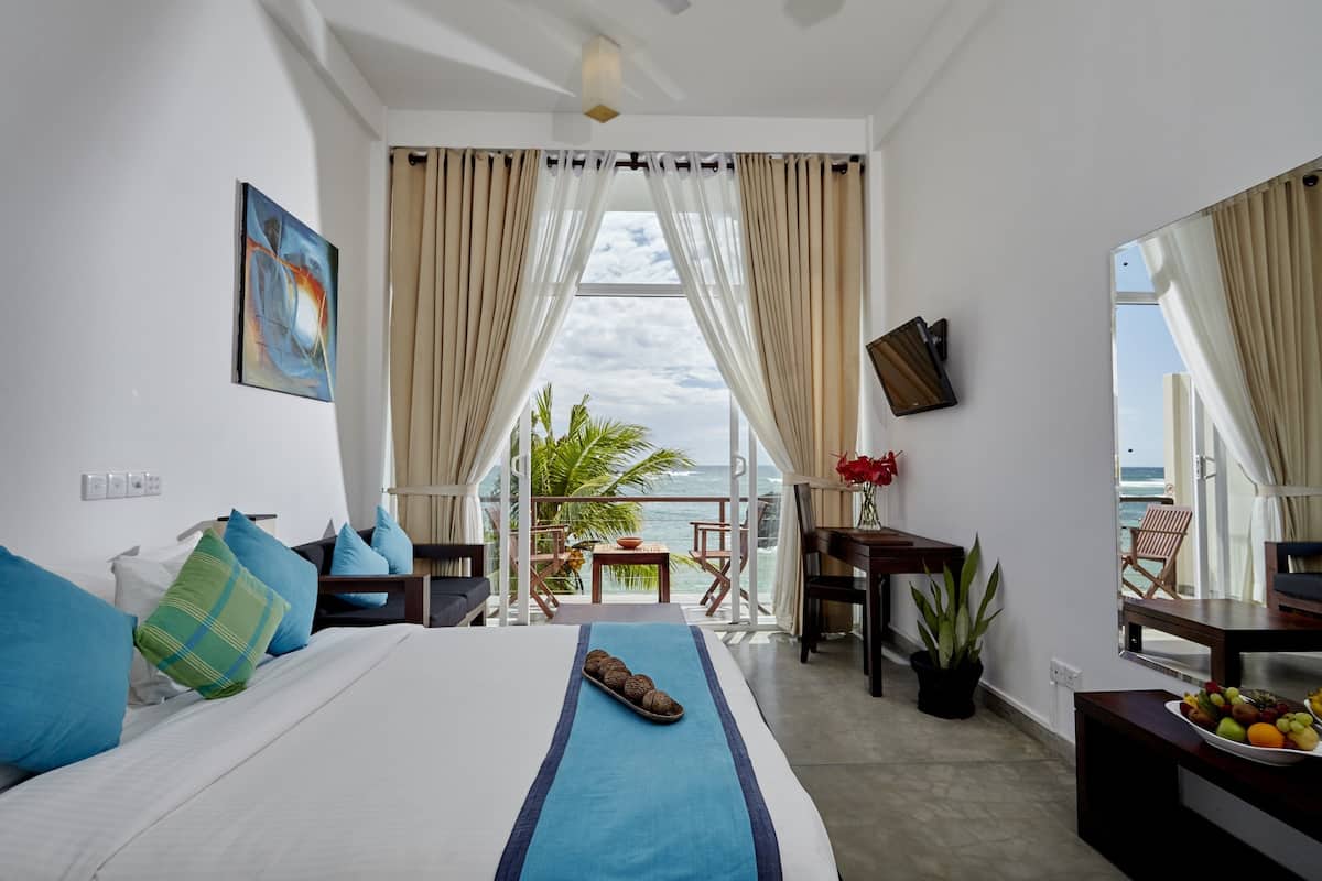 Habitación de hotel con cama, escritorio, silla, planta en maceta y vista al océano.