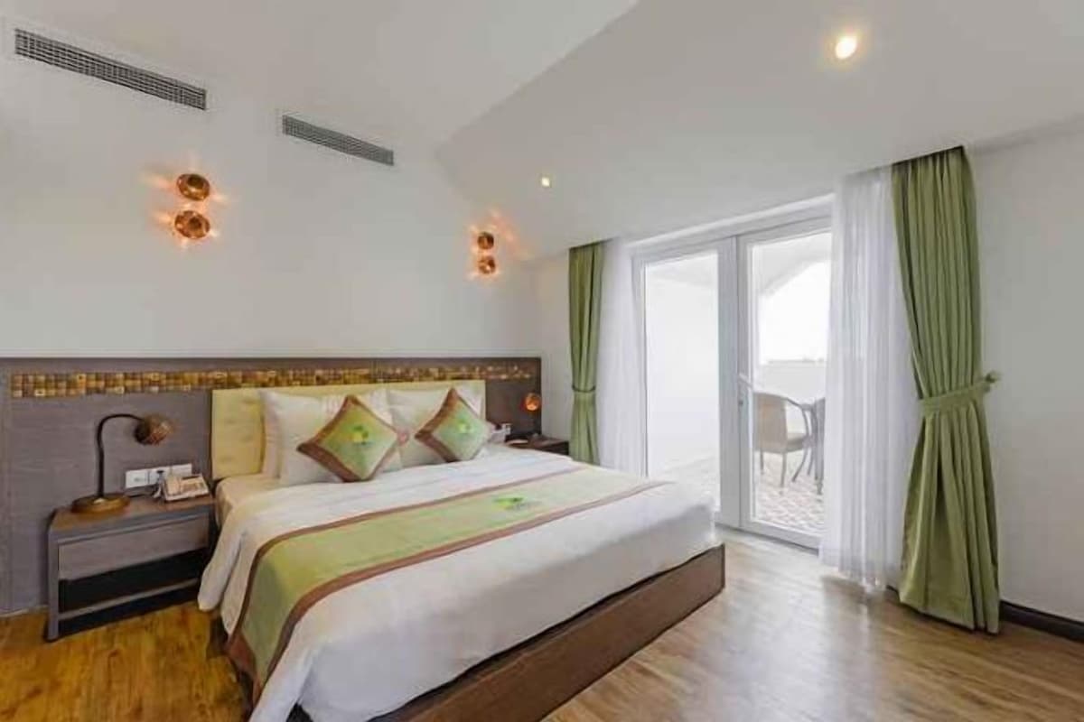 Quarto de hotel com uma cama grande, mesa de cabeceira, abajur e vista para o exterior.
