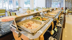 Ein reichhaltiges Buffet mit verschiedenen Speisen in Metallbehältern, präsentiert in einem großzügigen Speiseraum mit grünen Stühlen und Tischen.