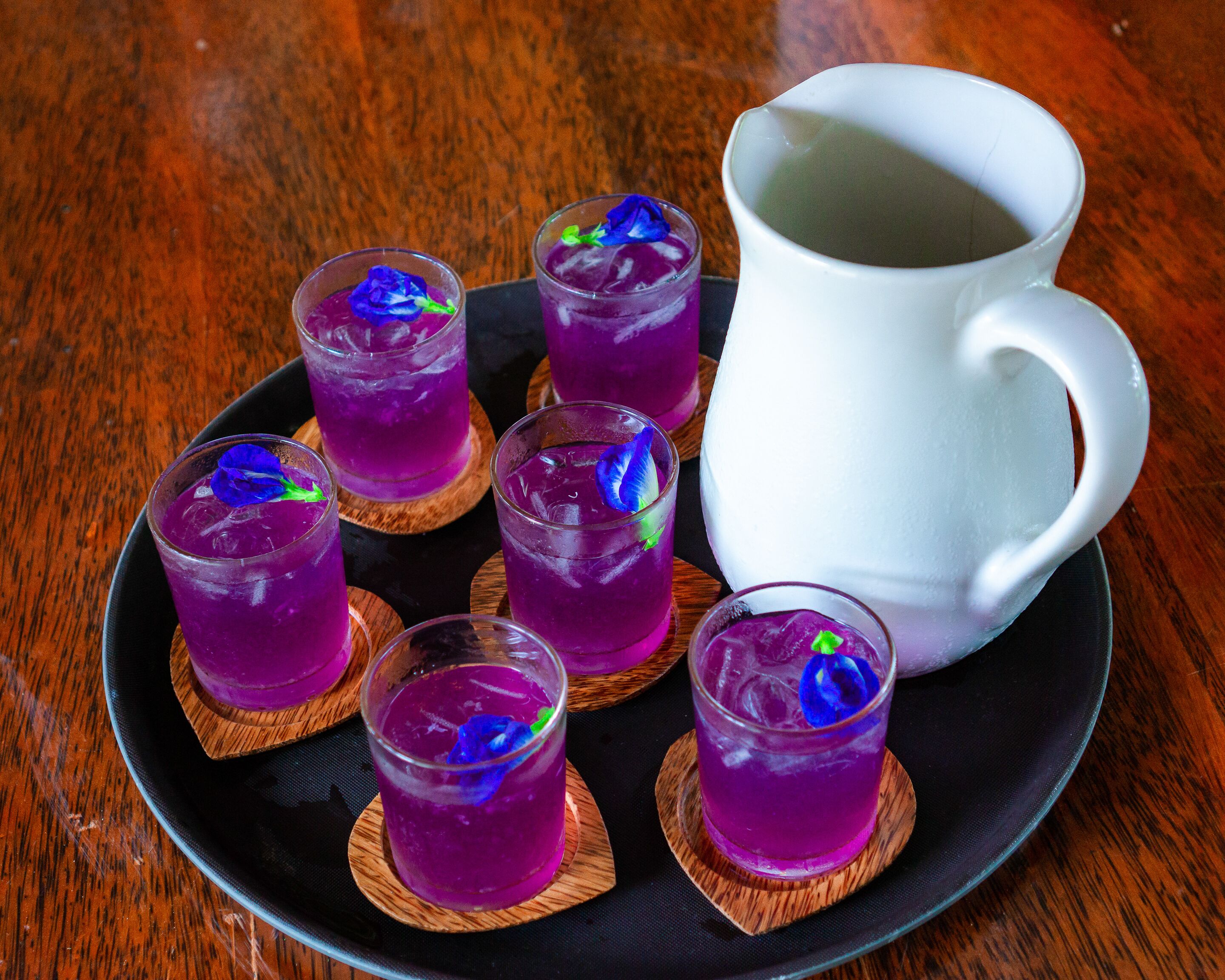 A table with six glasses of purple beverage, a white pitcher, and a black plate.