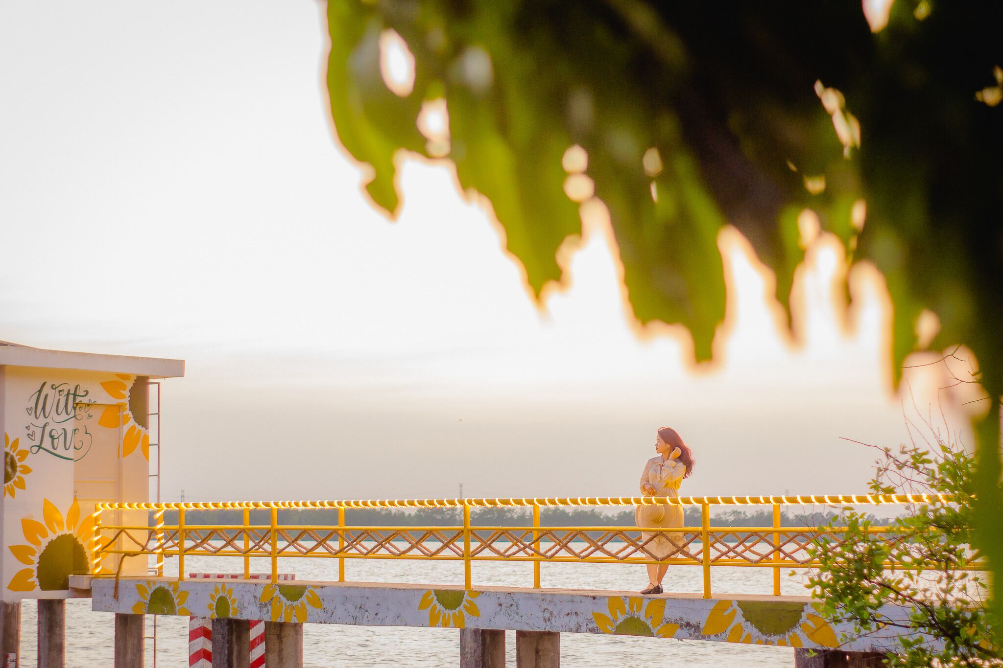 A pier with a yellow railing and a building with a sunflower mural and the words "With Love".
