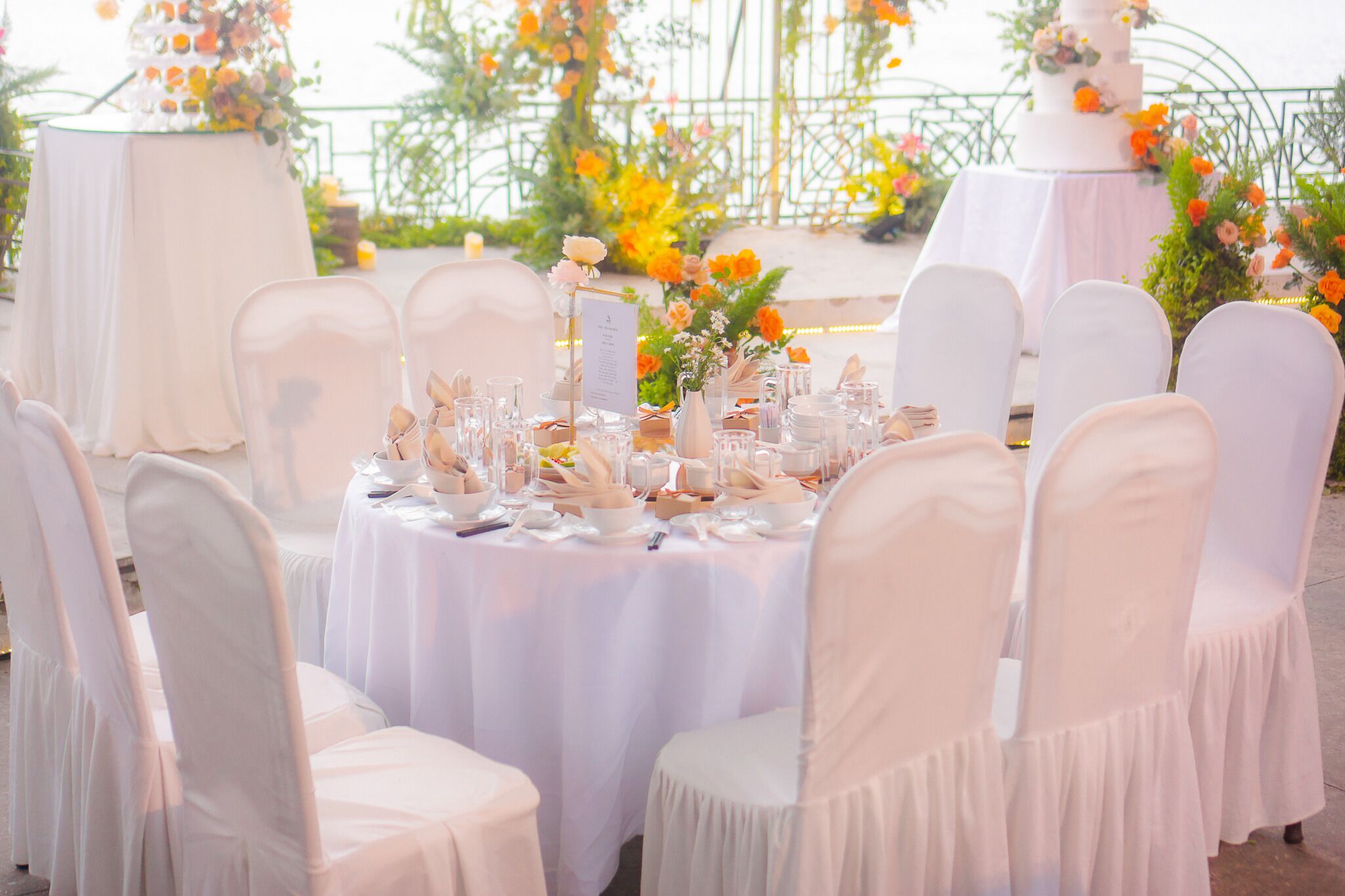 A wedding reception setup with round tables covered in white tablecloths, white chairs, and floral centerpieces.