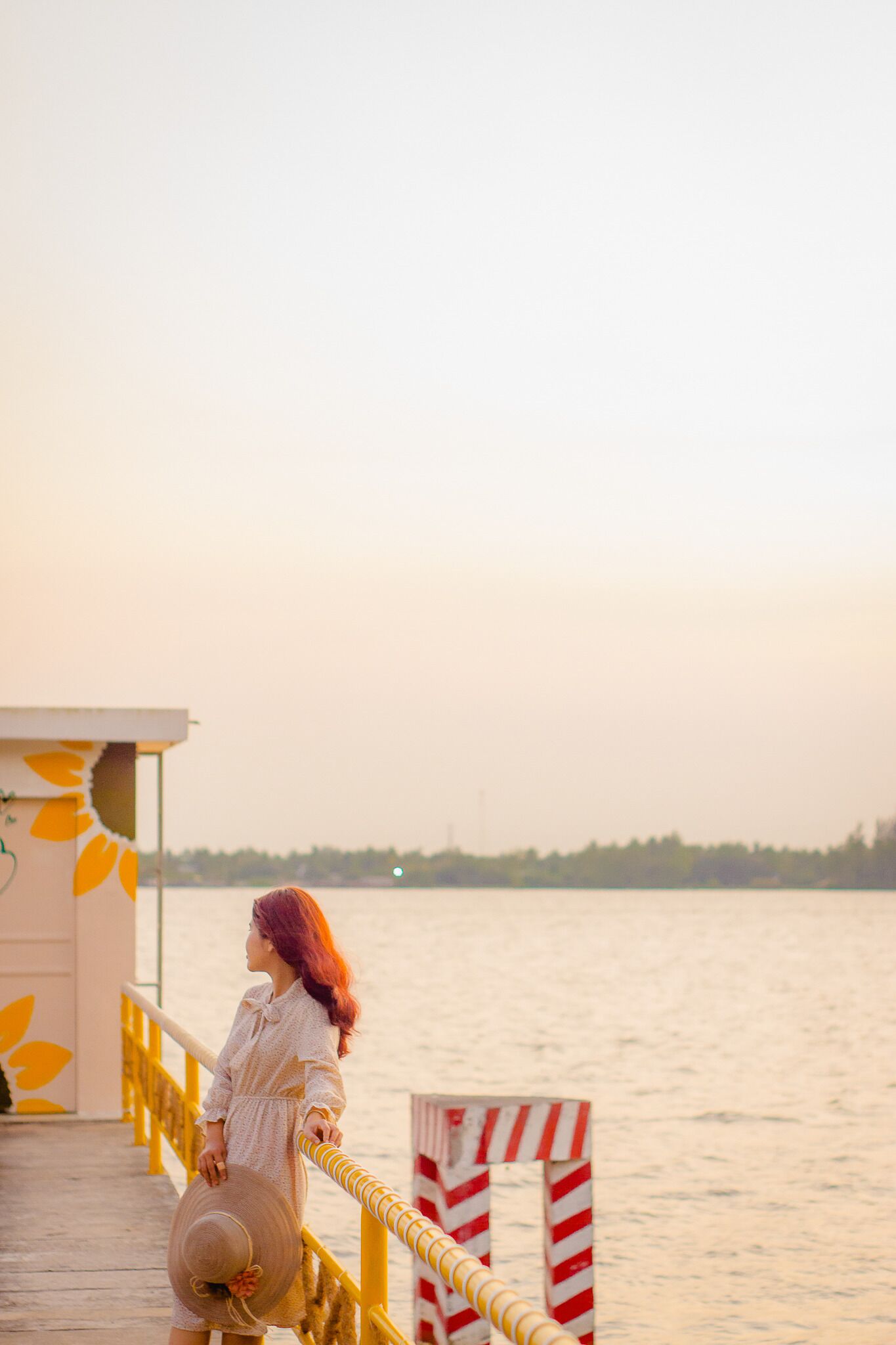 A woman standing on a wooden pier with a railing, overlooking a body of water.