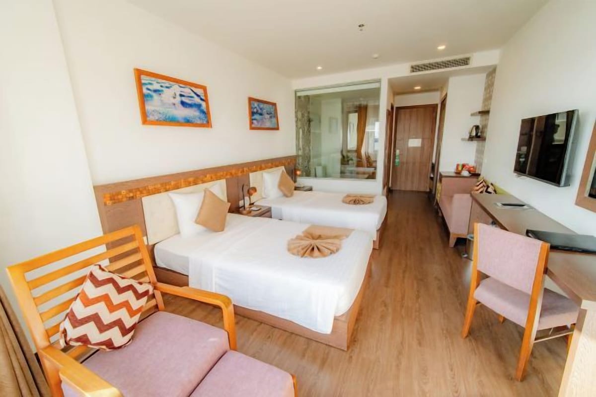 Une chambre d’hôtel avec deux lits, un bureau, une chaise et un téléviseur.
