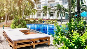 Ein Resort mit Pool, Holzliegen, Palmen und einem mehrstöckigen Gebäude.