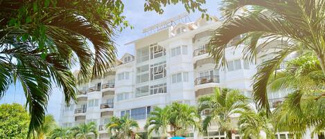 A hotel with a swimming pool surrounded by palm trees and blue umbrellas.