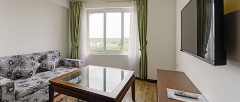 Una sala de estar moderna con un sofá, una mesa de centro de vidrio, un televisor de pantalla plana y una ventana con cortinas.